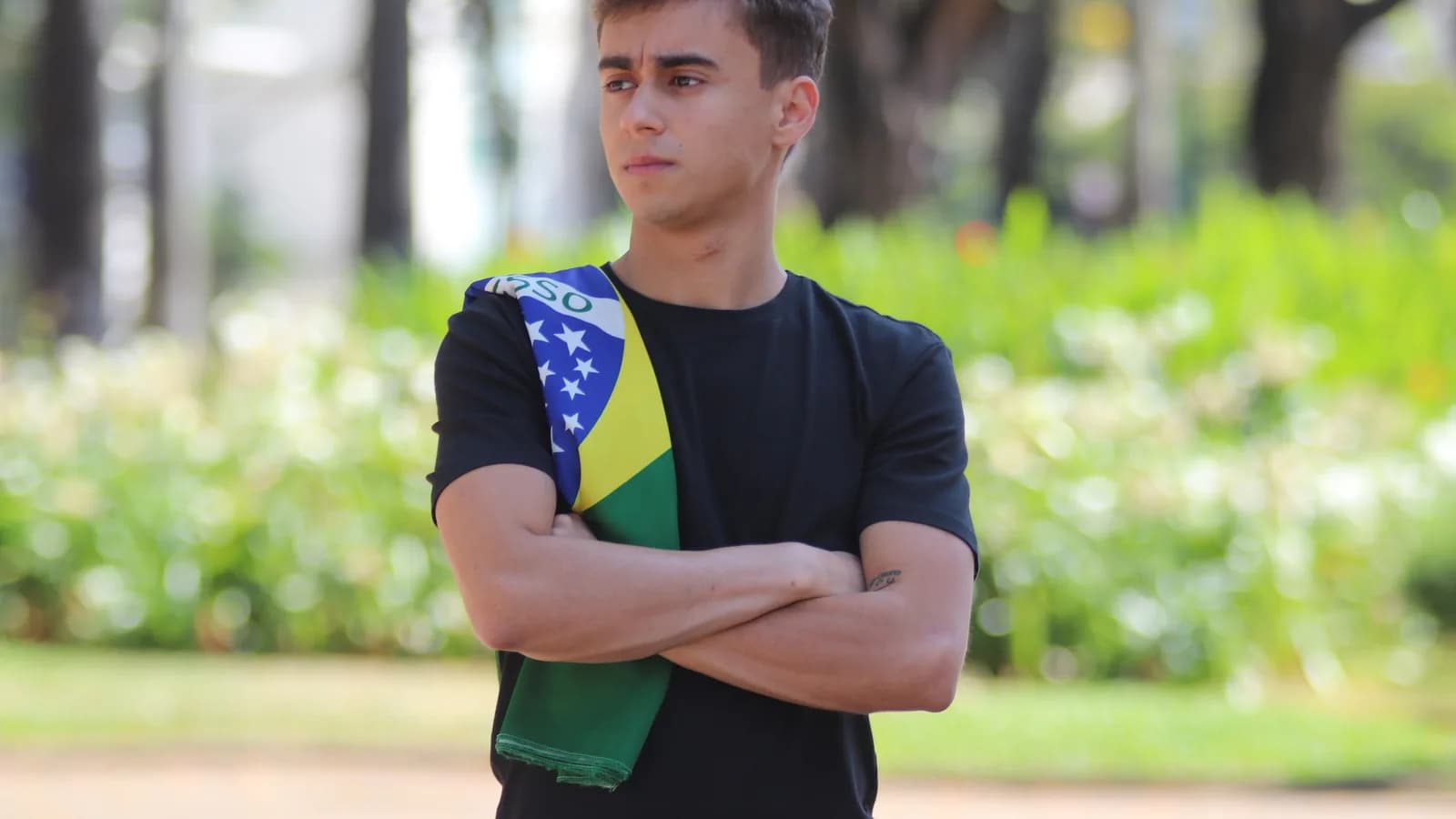 Nikolas Ferreira com braços cruzados usando bandeira do Brasil no ombro, foto de arquivo de 2020