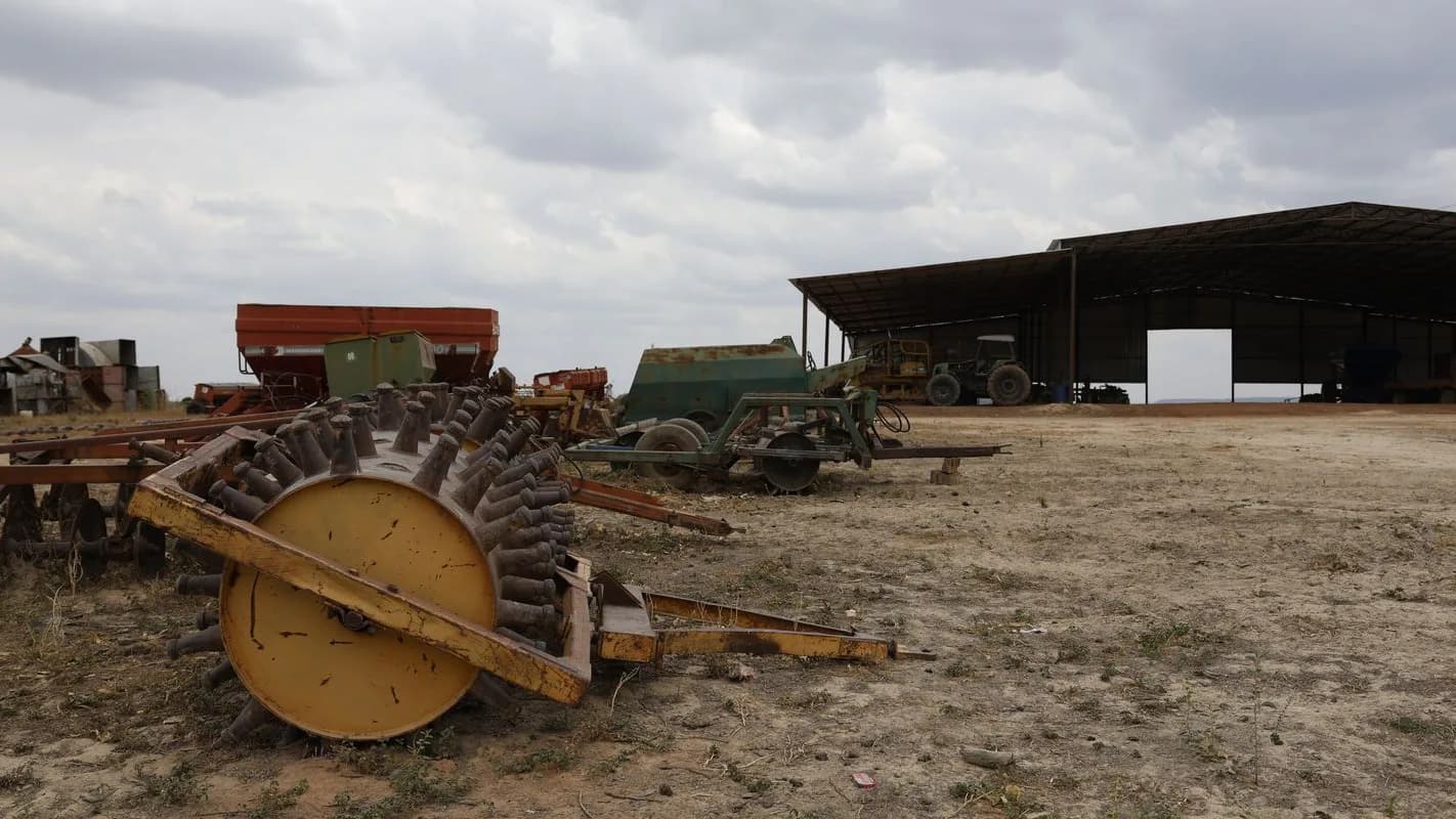 Maquinário agrícola parado em fazenda, com galpão ao fundo, imagem de arquivo