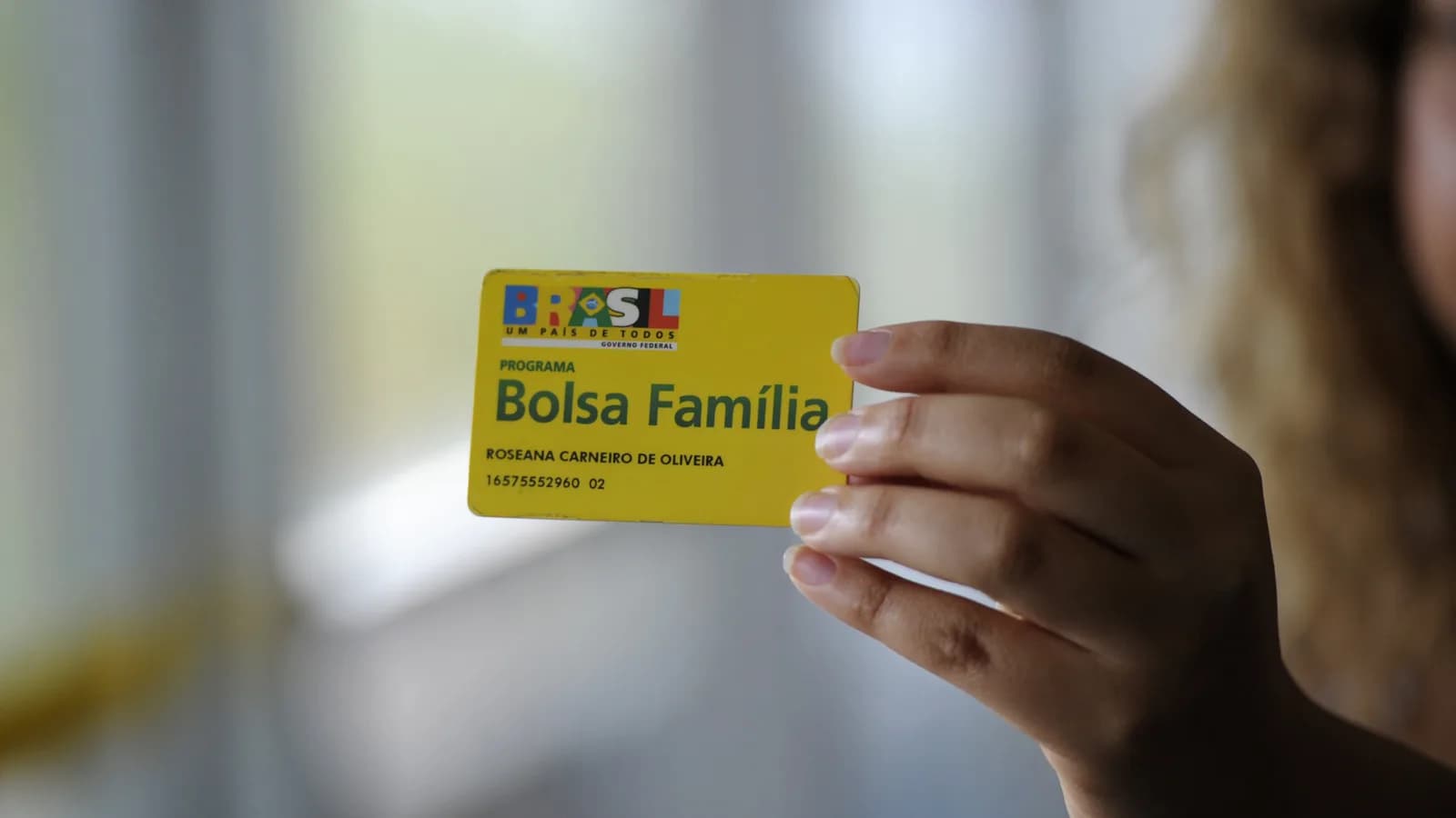 Mão segurando o cartão amarelo do Programa Bolsa Família