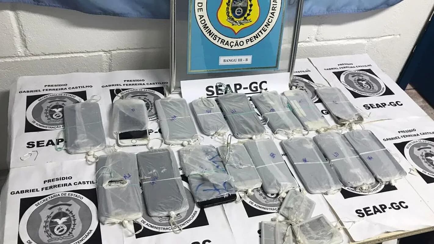 Celulares e outros materiais apreendidos em unidade prisional, organizados sobre mesa com etiquetas de identificação