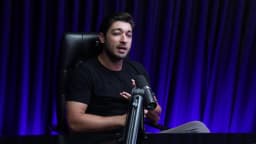 Rafael, fundador da Hoomy, gesticula durante entrevista sentado em cadeira gamer, diante de cortina azul