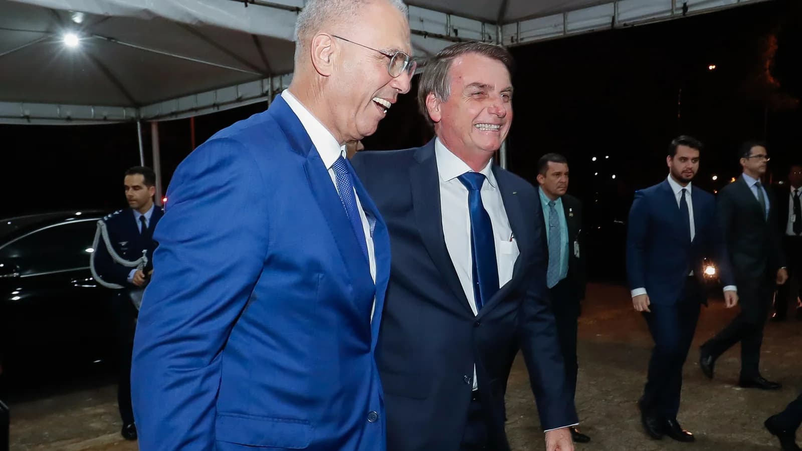 Jair Bolsonaro sorri ao lado de outro homem de terno em evento noturno, foto de arquivo de 2019