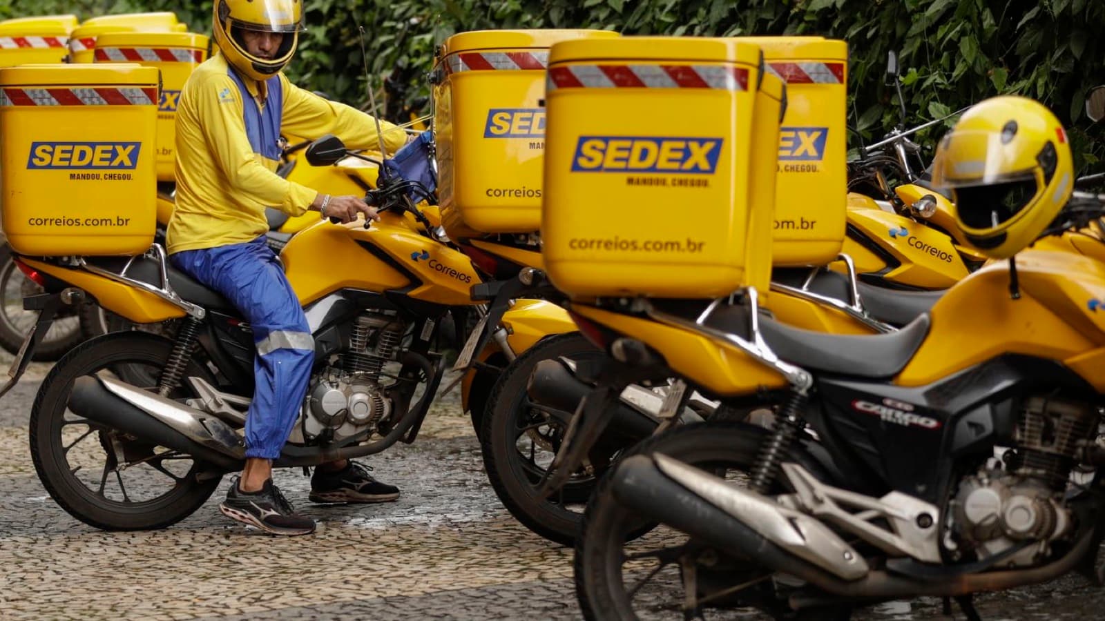 Carteiro dos Correios de capacete sobre motocicleta amarela com baús do Sedex, em imagem de arquivo