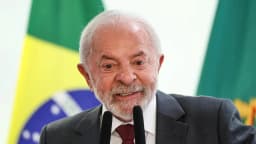 Presidente Lula sorri durante evento oficial, com bandeira do Brasil ao fundo