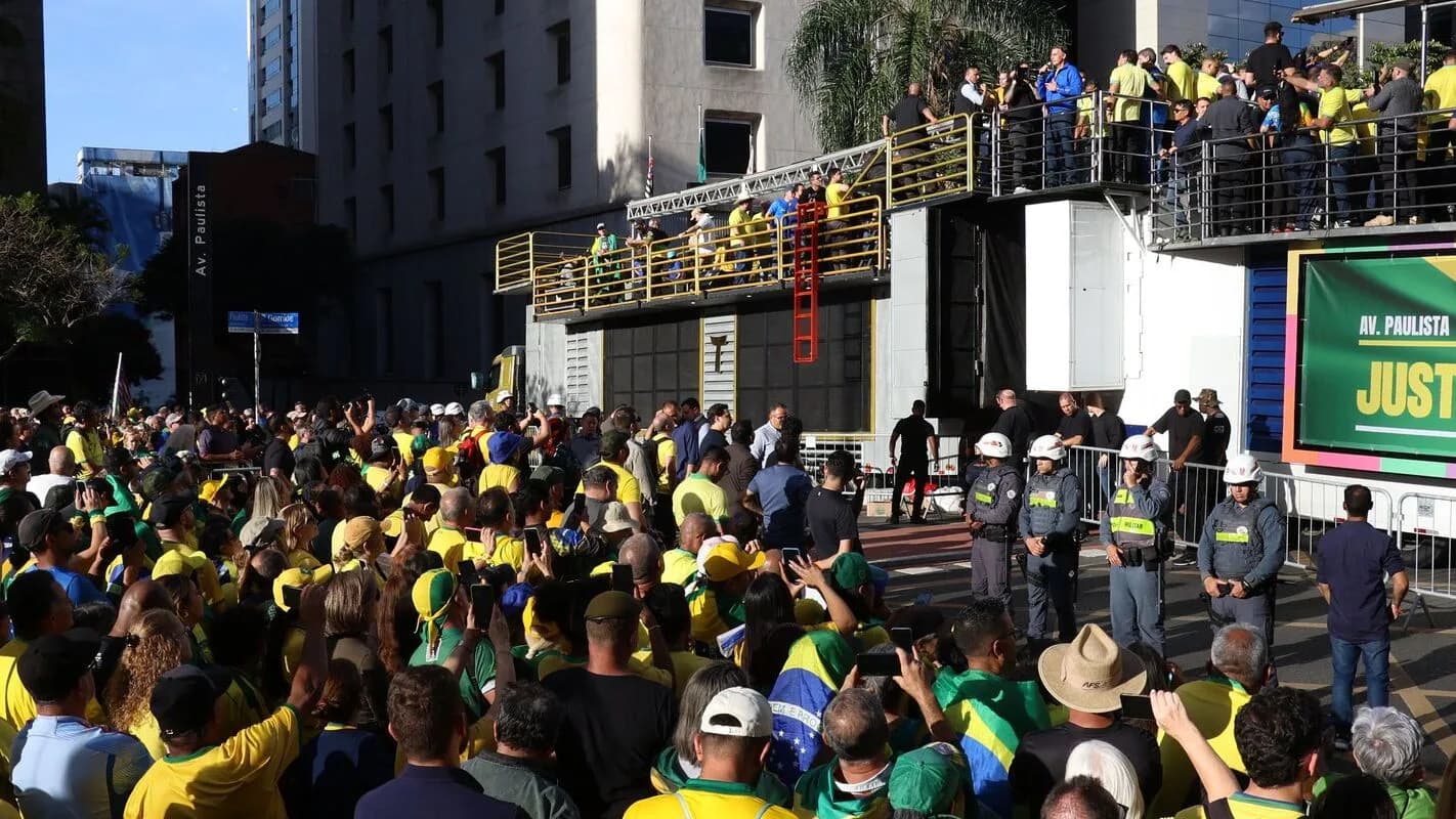 Multidão reunida em ato político em via pública de São Paulo, com faixas e bandeiras, cena semelhante às manifestações citadas no alerta britânico