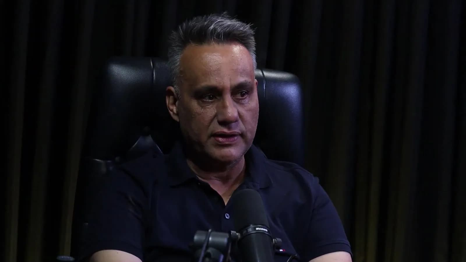 Rogério Furtado fala durante gravação do podcast Encampus, sentado em cadeira de couro preta contra fundo de cortina escura