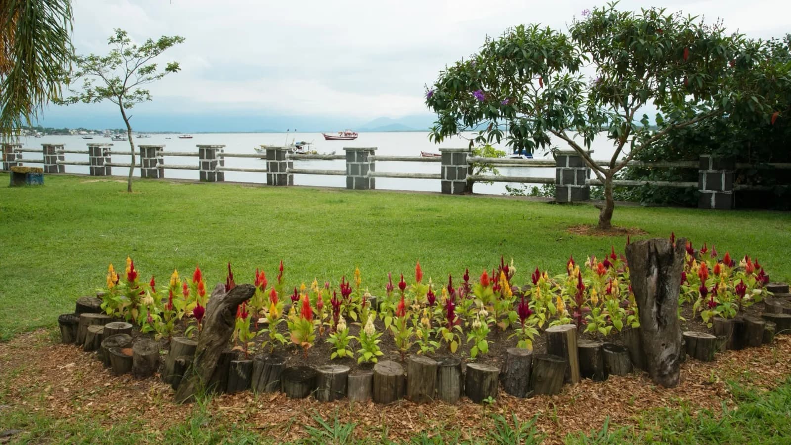 Vista da orla de Guaratuba, no litoral do Paraná, com barcos de pesca ancorados na baía e jardim à beira-mar