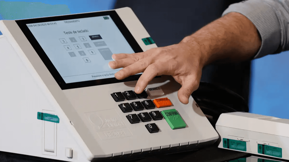 Mão testa o teclado de uma urna eletrônica durante demonstração do TRE para as Eleições 2026