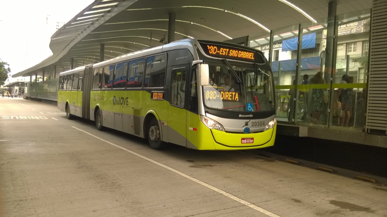Ônibus articulado verde do sistema MOVE parado em estação do transporte coletivo de Belo Horizonte, com passageiros aguardando na plataforma