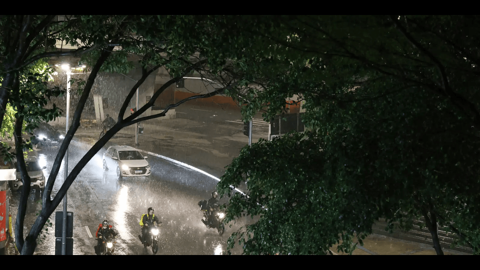 Motociclistas e carro trafegam por avenida durante forte chuva noturna (imagem de arquivo, chuva em São Paulo)
