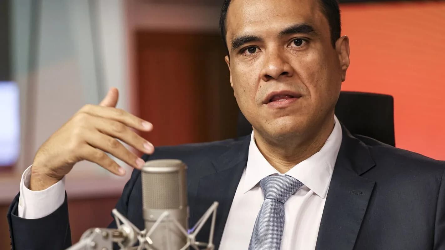 Gustavo Feliciano, ministro do Turismo, gesticulando durante entrevista com microfone à frente