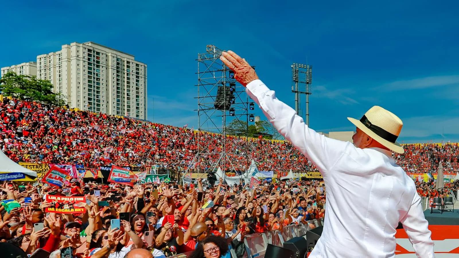 Lula acena de costas para multidão durante lançamento oficial da campanha, em estádio lotado com bandeiras vermelhas