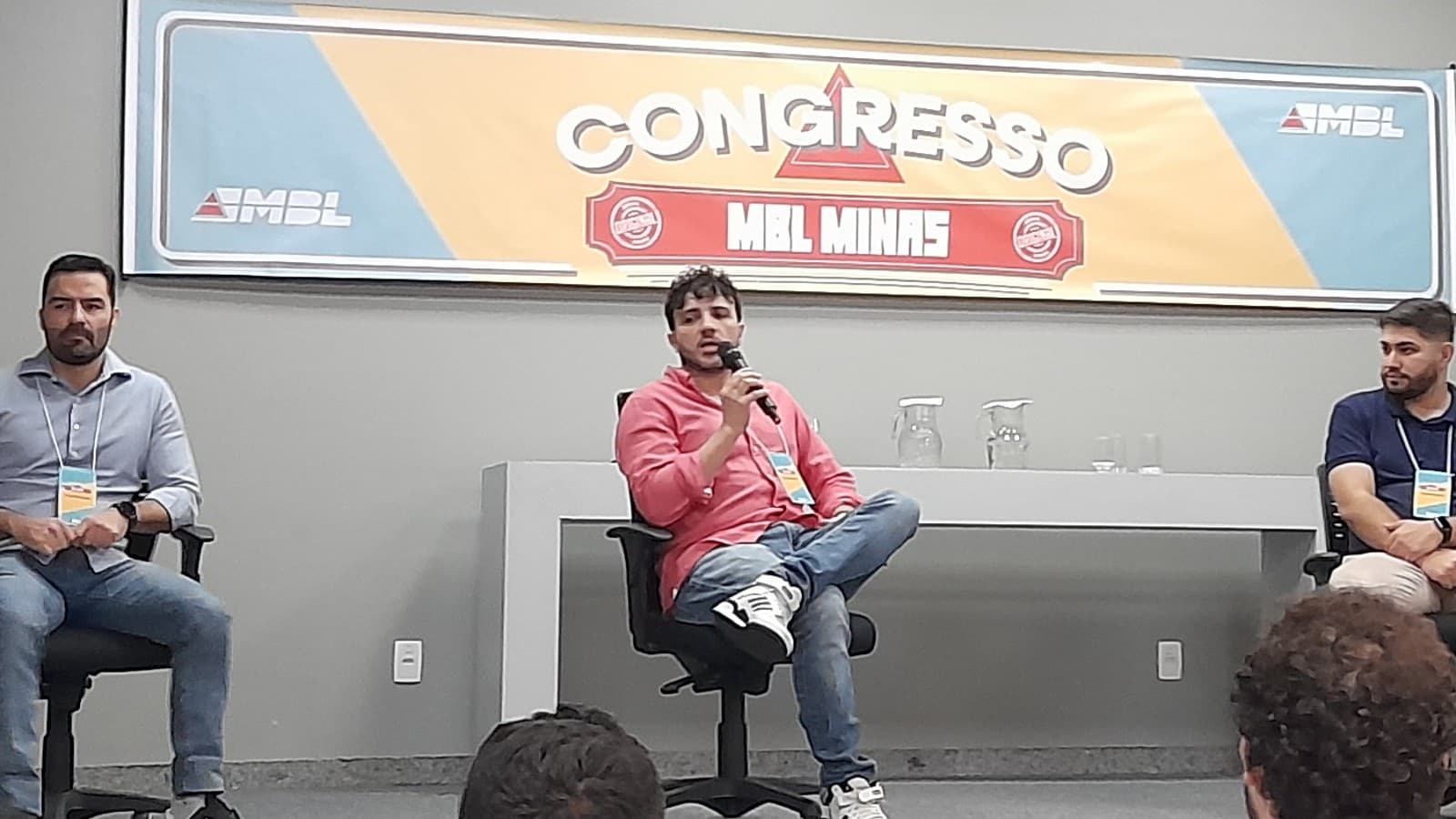 Renan Santos discursando com microfone em evento do MBL, sentado ao lado de outros participantes de painel