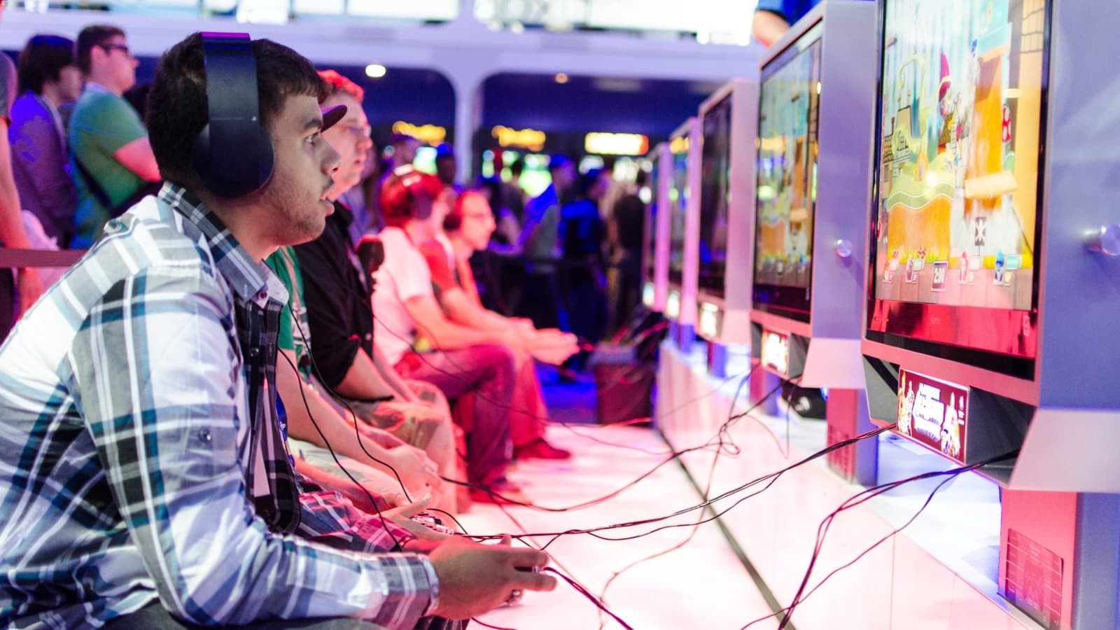 Jogadores usando fones de ouvido e controles em consoles de videogame durante feira de games, foto de arquivo