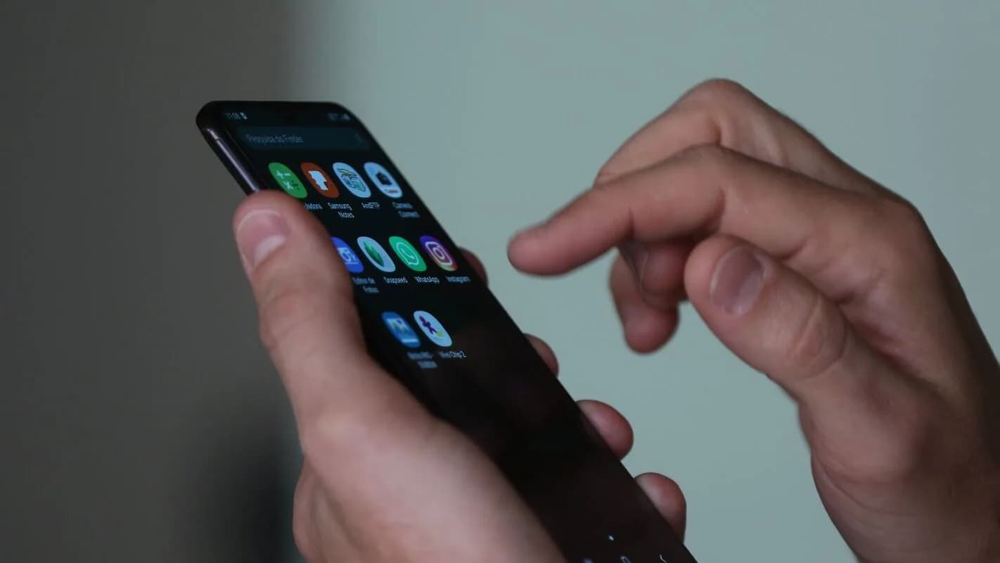 Close de mãos usando um smartphone com ícones de aplicativos na tela