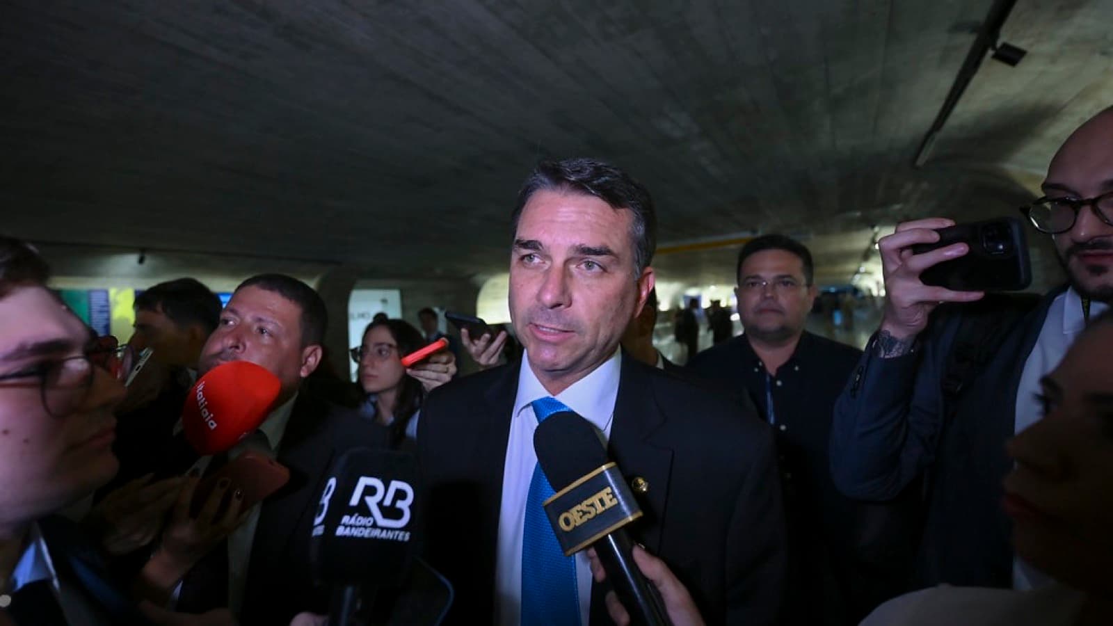 Senador Flávio Bolsonaro concede entrevista a jornalistas cercado de microfones