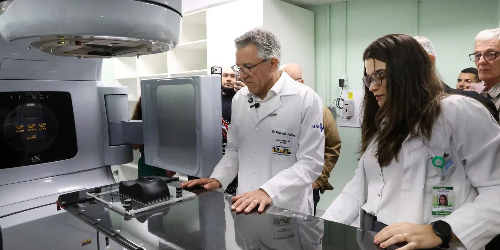 Ministro Alexandre Padilha, de jaleco branco, examina equipamento médico ao lado de uma profissional de saúde durante visita a hospital universitário