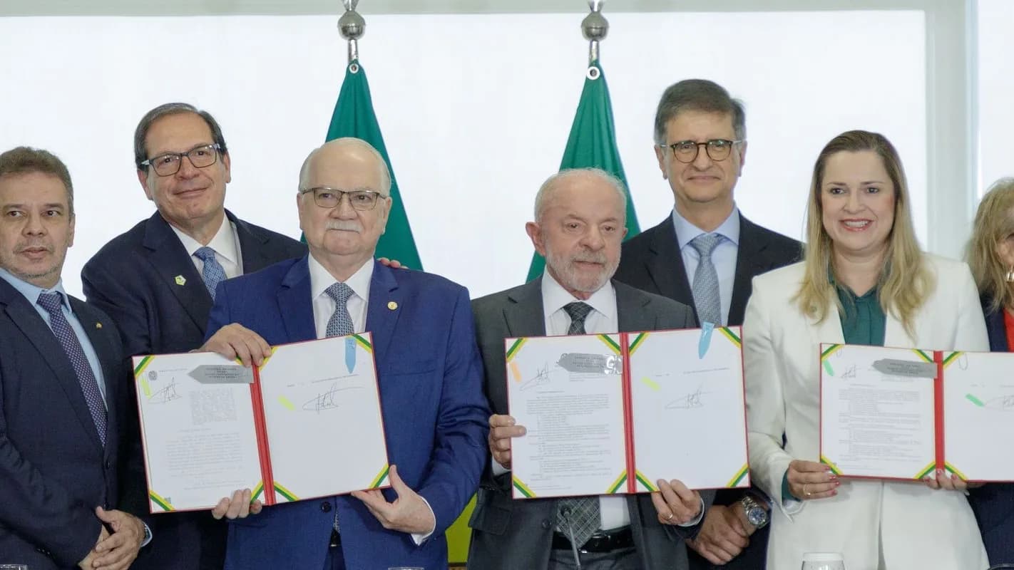 Lula e o ministro Edson Fachin posam lado a lado segurando documentos assinados em cerimônia no Planalto, cercados por outras autoridades