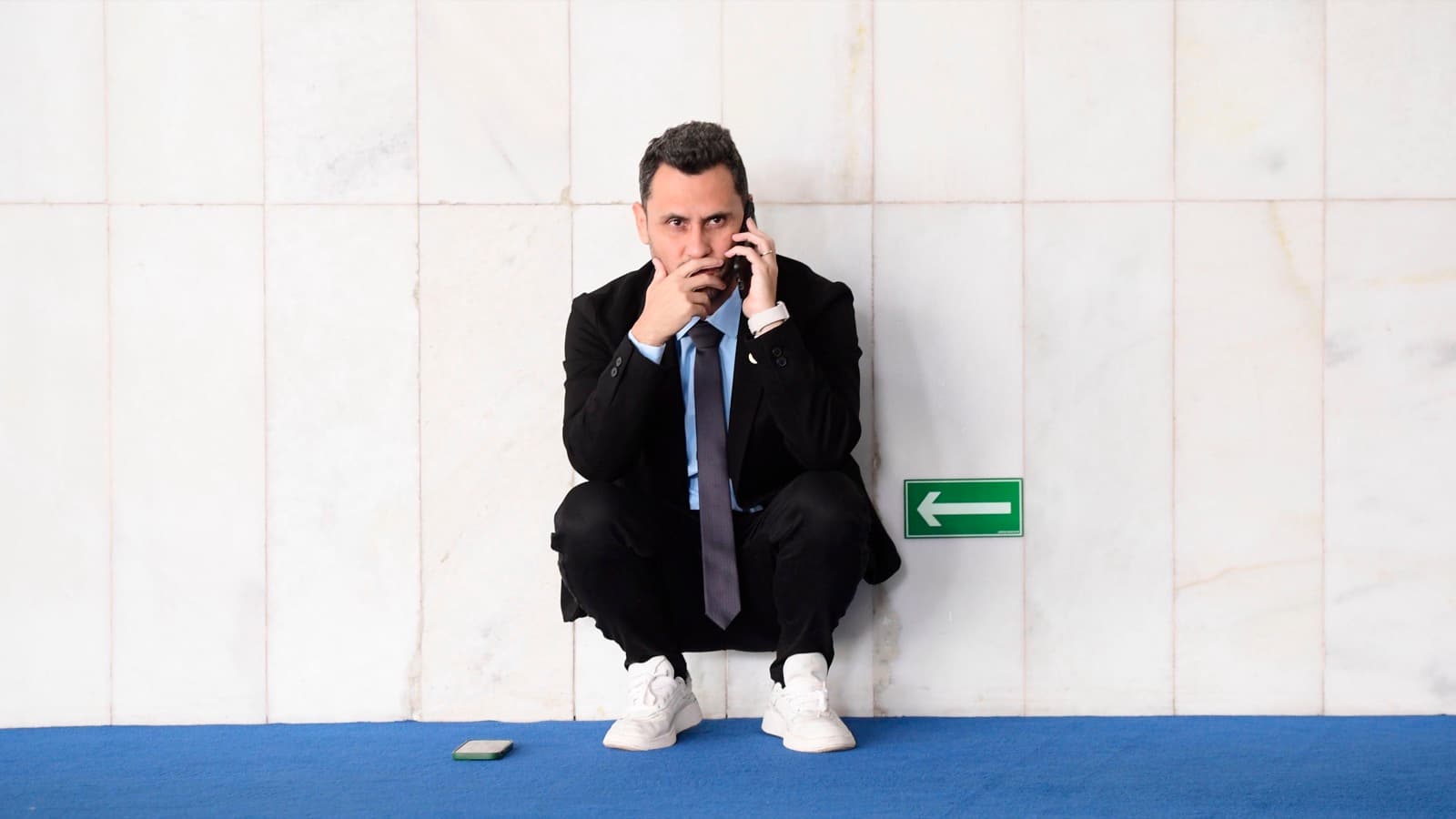 O senador Cleitinho, de terno escuro e tênis brancos, agachado junto a uma parede de mármore enquanto fala ao celular no Senado, em foto de arquivo de abril de 2025