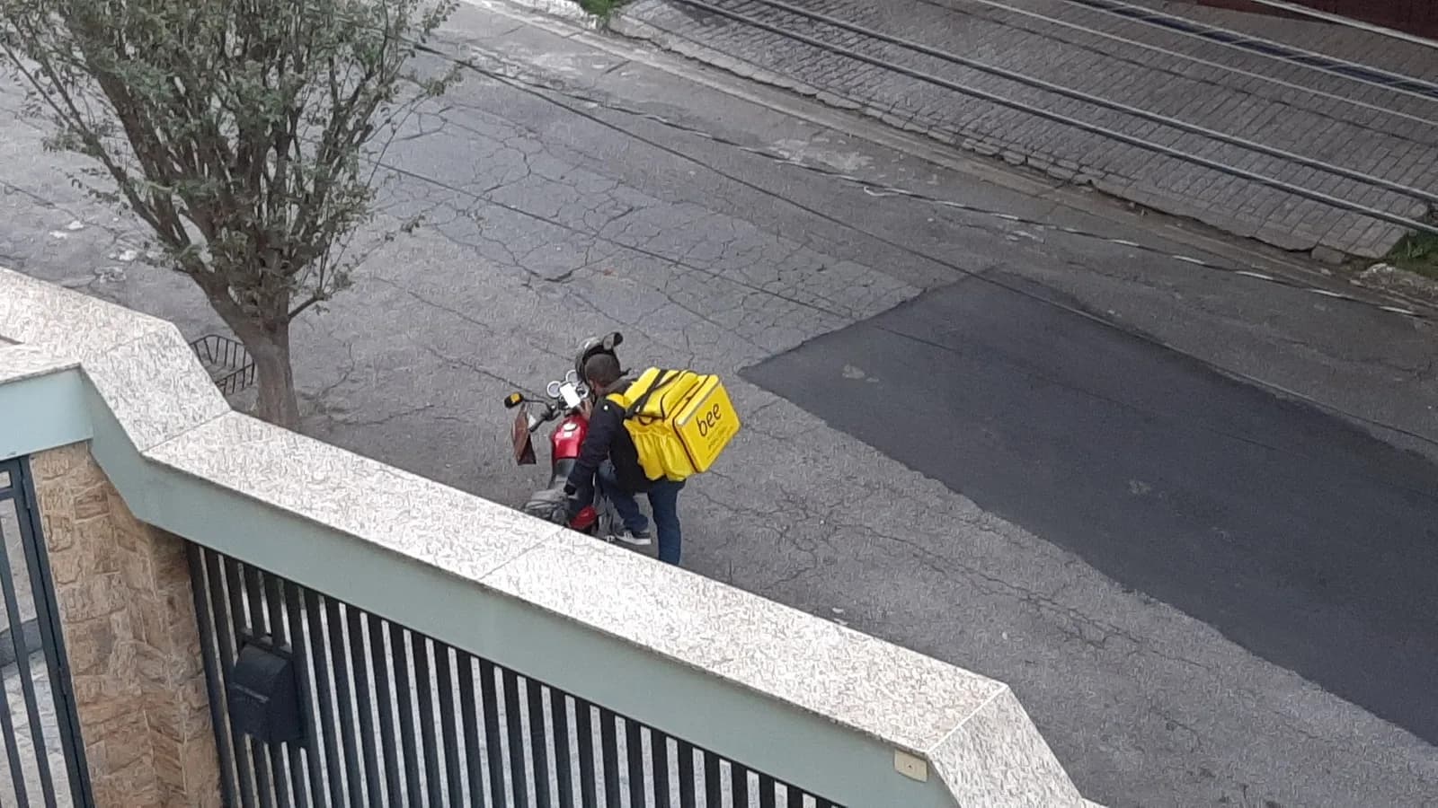 Entregador de aplicativo visto de cima pedalando por rua durante o dia